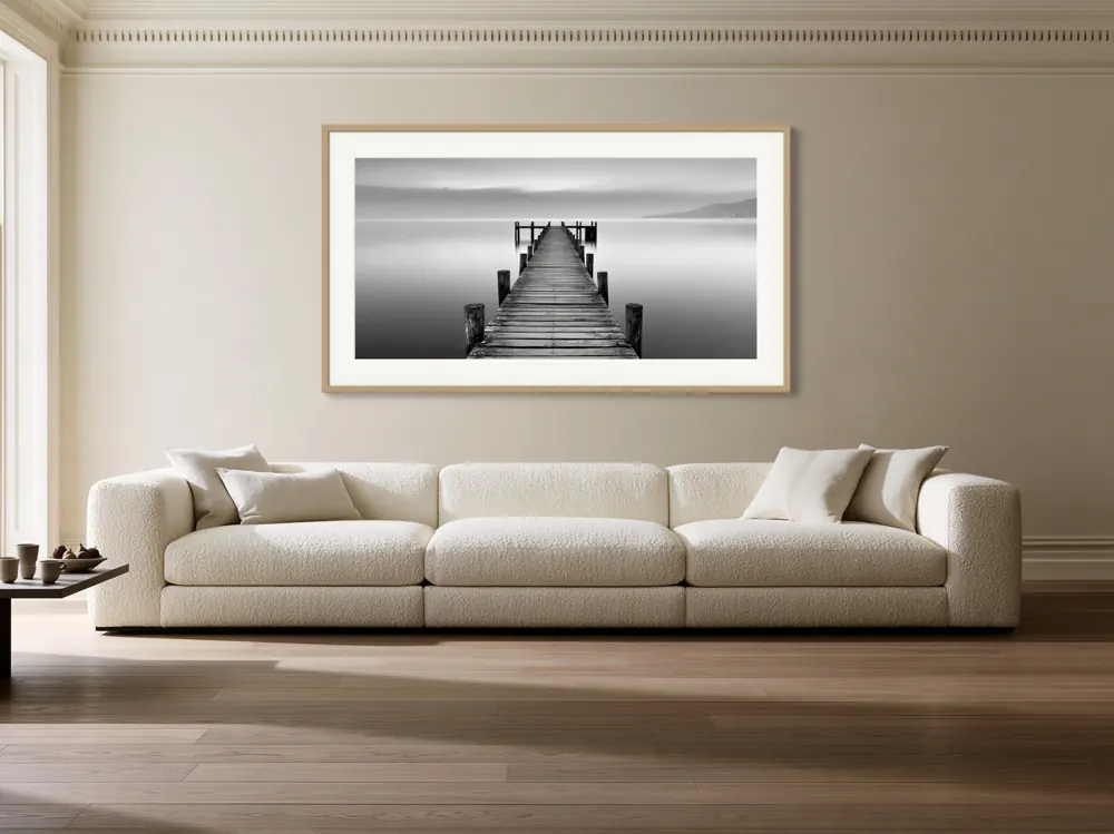 A black-and-white lake pier photograph as a natural oak framed print with a white mat in the Cornice bouclé living