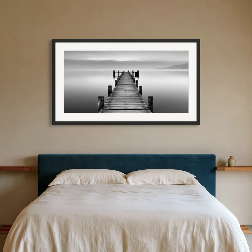 A black-and-white lake pier photograph as a black framed print with a white mat in the Indigo bedroom