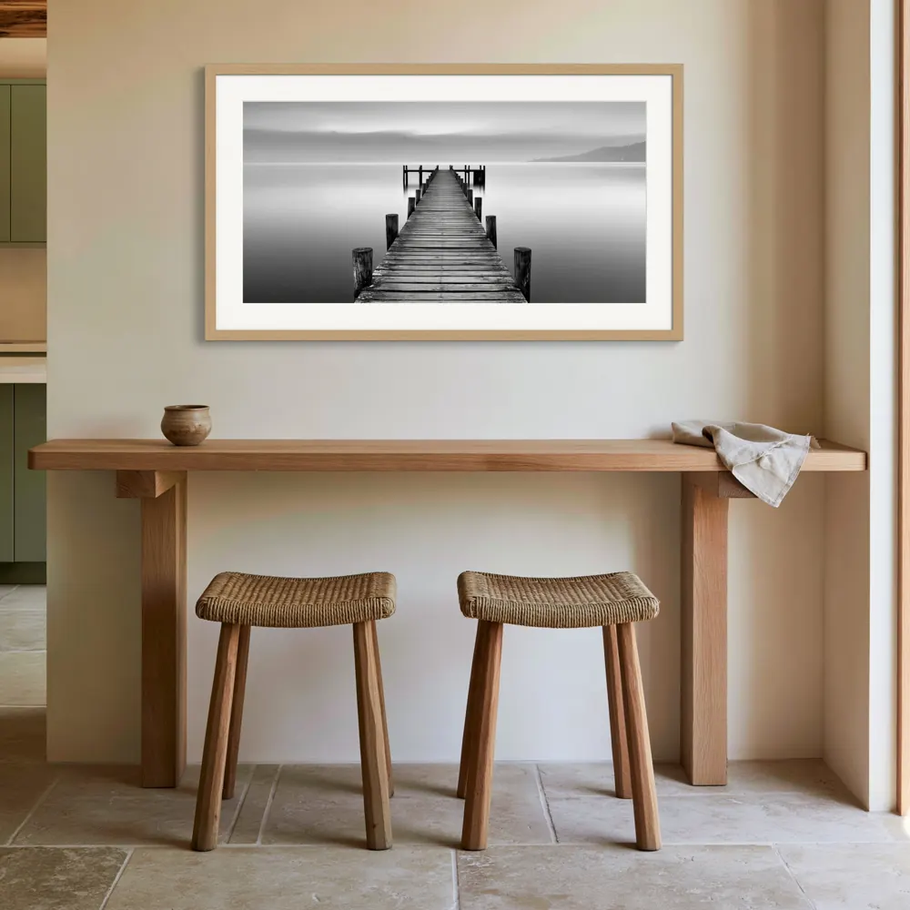 A black-and-white lake pier photograph as a natural oak framed print with a white mat in the Ivory kitchen breakfast ledge